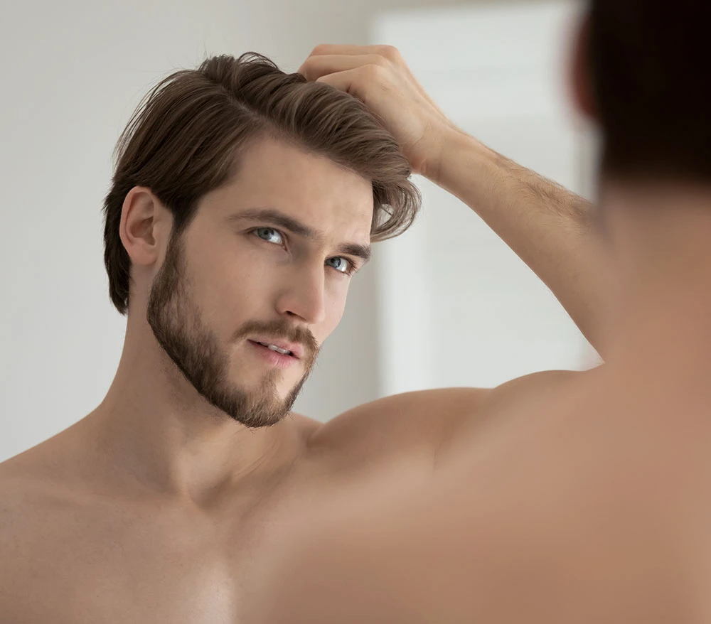 handsome man playing with hair in the mirror | Raggio Facial Plastic Surgery